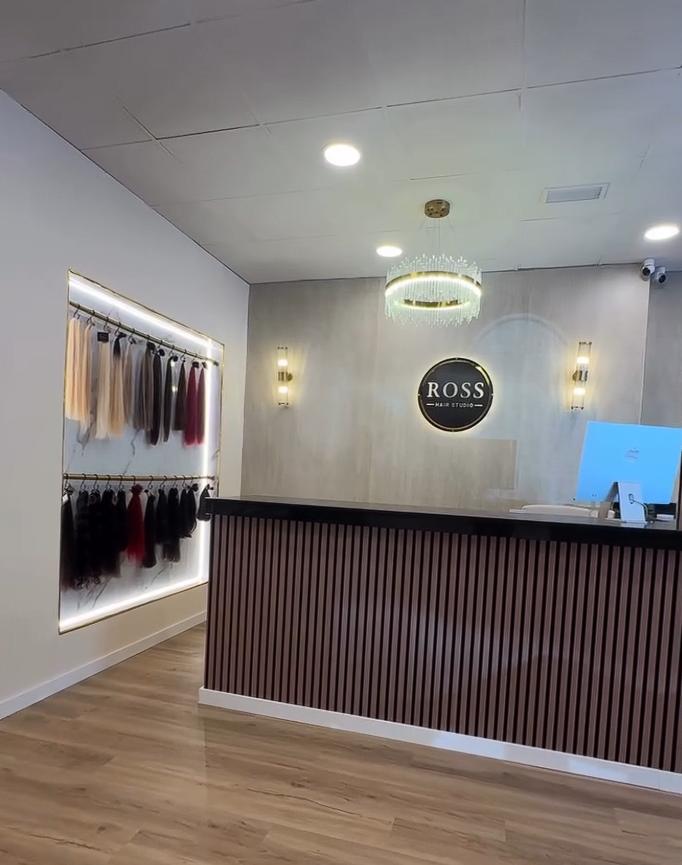 Recepción de Ross Hair Studio con el muro iluminado de extensiones, la lámpara de cristal y el logo en la pared