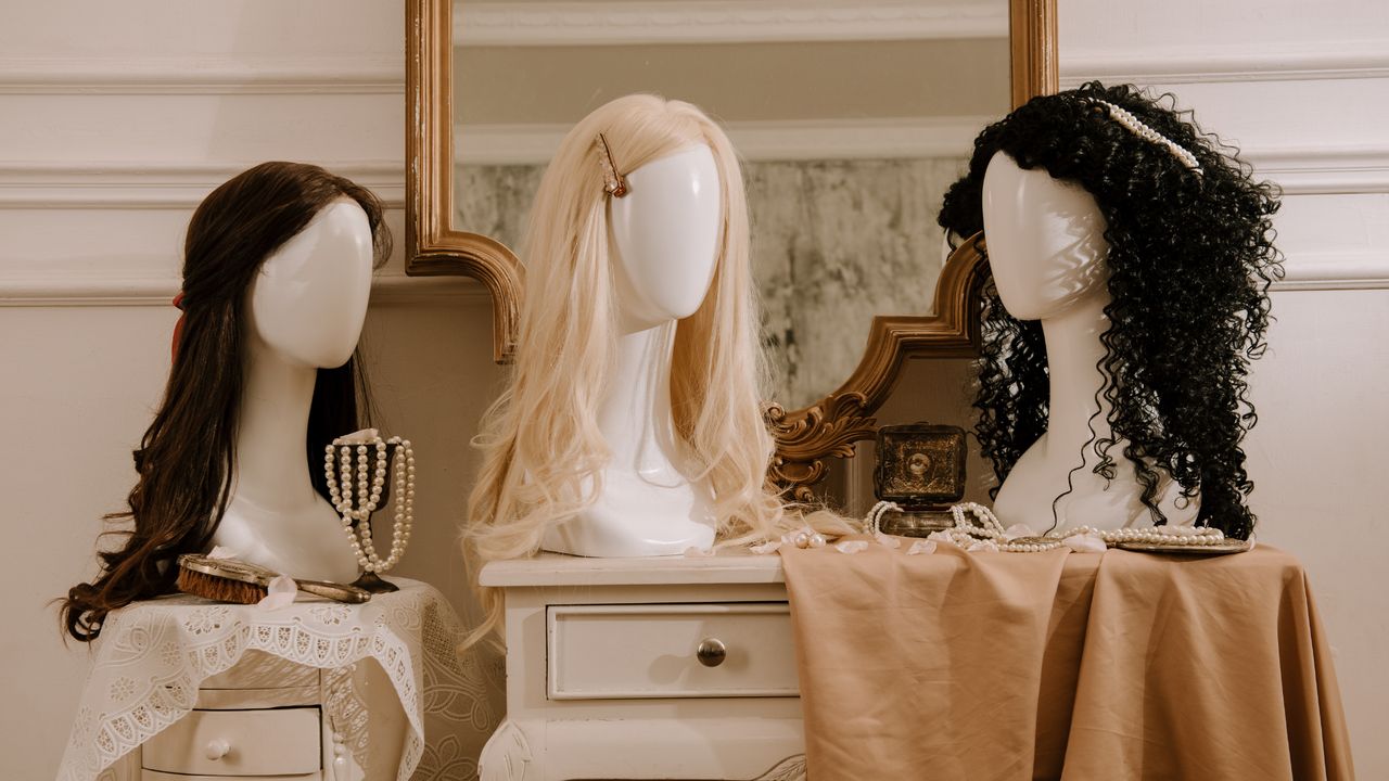 Tres pelucas sobre cabezas de maniquí: castaña ondulada, rubia larga y negra rizada
